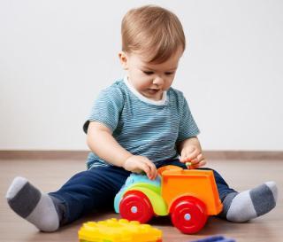 A young white boy playing with a colourful plastic truck